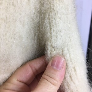 K&ouml;nnte beinhalten: Nahaufnahme eines wei&szlig;en, flauschigen Strickpullovers, der die Textur des Stoffes zeigt.