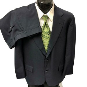May include: A dark blue suit with a single-breasted jacket and matching pants. The jacket has a two-button closure and a notch lapel. The suit is made of a smooth, woven fabric.