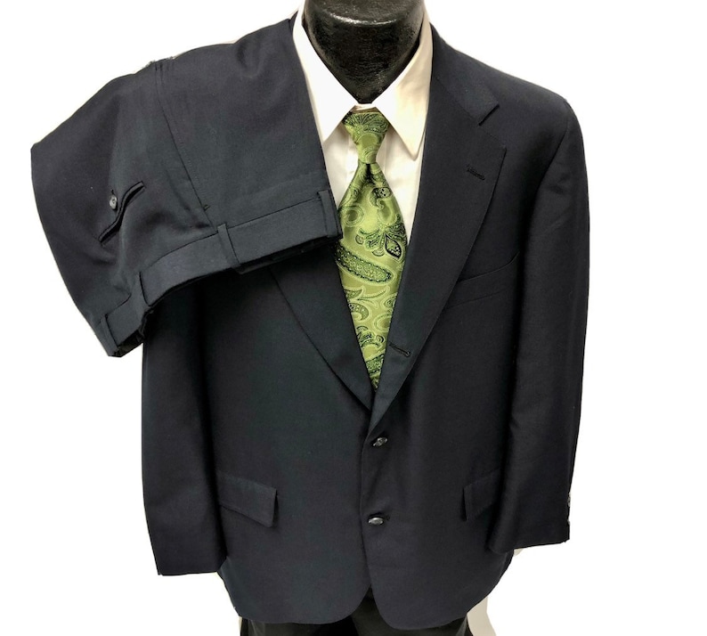 May include: A dark blue suit with a single-breasted jacket and matching pants. The jacket has a two-button closure and a notch lapel. The suit is made of a smooth, woven fabric.