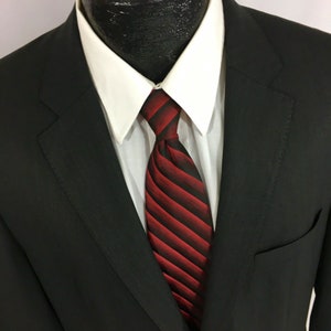 May include: A black suit jacket with a white shirt and a red and black striped tie.