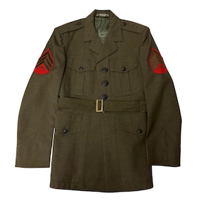 May include: A green military jacket with a belt and two pockets on the front. The jacket has red and green insignia on the sleeves.