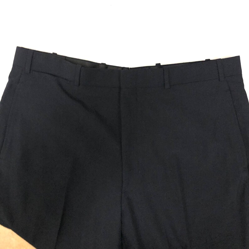 May include: A pair of dark blue dress pants with a flat front and a belt loop waistband.