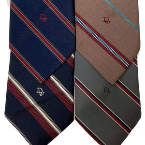 May include: Three striped neckties with the Dior logo embroidered on each. The ties are navy blue with red and white stripes, brown with red and blue stripes, and grey with red and white stripes.