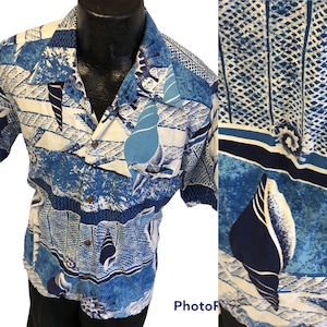 Pode incluir: Uma camisa branca e azul de manga curta com botões e um padrão de conchas. A camisa tem um bolso no lado esquerdo e uma gola com padrão azul e branco.