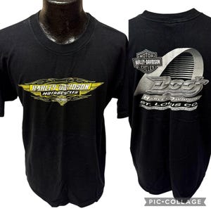 May include: Black Harley-Davidson t-shirt. The front features a yellow and black Harley-Davidson Motorcycles logo. The back displays a silver and white graphic with the text "Dog's Harley-Davidson St. Louis Co."