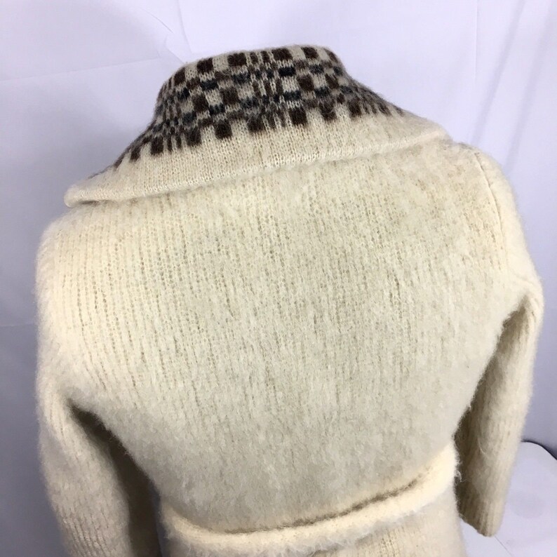 K&ouml;nnte beinhalten: Ein wei&szlig;er Strickcardigan mit einem braunen und schwarzen karierten Kragen. Der Cardigan hat lange &Auml;rmel und einen Bindeg&uuml;rtel.