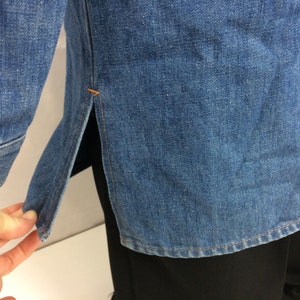 Puede incluir: Una camisa vaquera azul con un detalle de costura lateral. La camisa tiene manga larga y un frente abotonado.