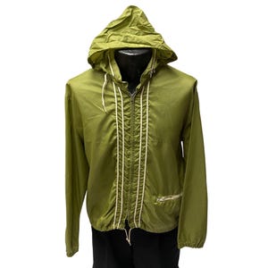 Puede incluir: Una chaqueta verde con capucha, cordones blancos y cierre de cremallera. La chaqueta tiene un pequeño bolsillo en el lado izquierdo.