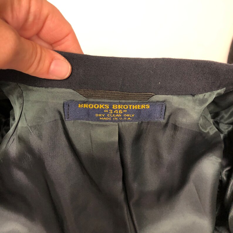 May include: A navy blue Brooks Brothers label with gold lettering. The label reads "Brooks Brothers" "346" "Dry Clean Only" "Made in U.S.A."