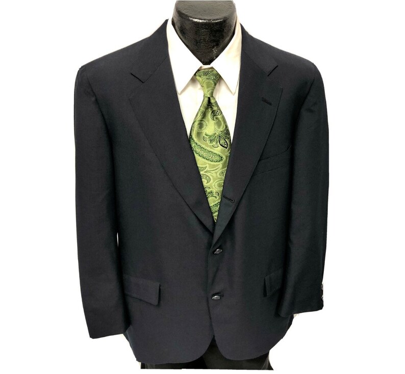 May include: A dark blue blazer with a three-button closure and a single vent in the back. The blazer has a green paisley patterned tie.
