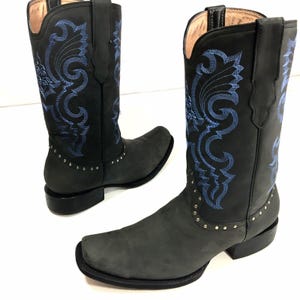 May include: A pair of black leather cowboy boots with blue embroidery. The boots have a pointed toe and a stacked heel. The boots are decorated with silver studs.