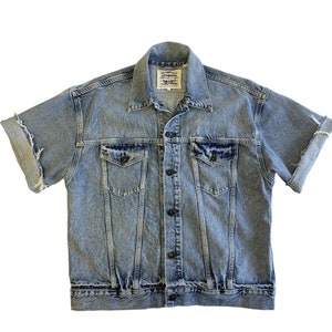 May include: A light blue denim jacket with short sleeves and a button-up front. The jacket has two chest pockets and a Levi's label on the left side.