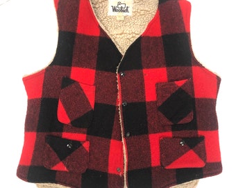 Könnte beinhalten: Rote und schwarze karierte Fleece-Weste mit Knopfleiste und zwei Fronttaschen. Die Weste hat ein "Woolrich"-Etikett.