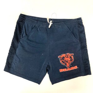 May include: Navy blue athletic shorts with mesh side panels and a Chicago Bears logo on the right leg. The logo is orange and red with the word "BEARS" in white.