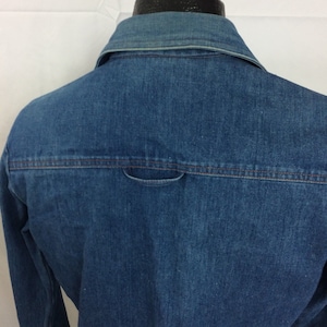 Puede incluir: Una camisa vaquera azul con un solo bolsillo trasero. La camisa tiene cuello abotonado y mangas largas.