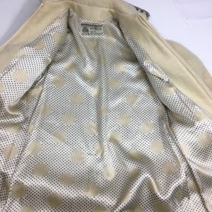 K&ouml;nnte beinhalten: Eine cremefarbene Jacke mit Rei&szlig;verschluss und einem Tupfenfutter. Das Futter ist ein cremefarbener Satin mit schwarzen Tupfen. Die Jacke hat ein Etikett mit der Aufschrift "Icewool" mit dem Text "100% Reine Schurwolle" und "Hergestellt in Schottland".