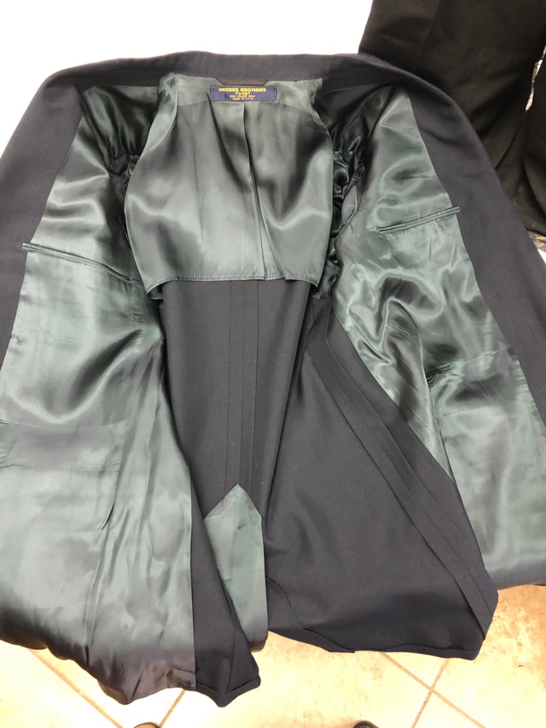 May include: The inside of a navy blue blazer with a green satin lining. The label reads "Brooks Brothers" with the text "Made in USA" underneath.