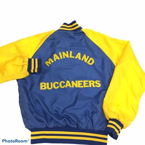 Pode incluir: Uma jaqueta de beisebol de cetim azul e amarela com o texto "Mainland Buccaneers" nas costas.