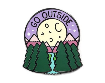May include: A purple and white enamel pin with the text "GO OUTSIDE" and a cartoon moon with stars and mountains. The mountains are pink and the trees are green.