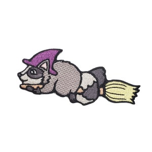 May include: Embroidered iron-on patch of a cartoon raccoon wearing a purple witch hat and riding a yellow broom.