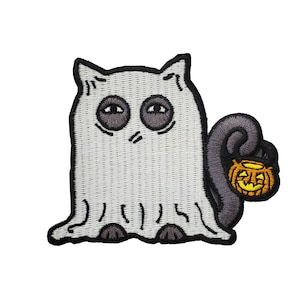 May include: A white ghost with black eyes and a black tail holding a small orange jack-o'-lantern. The ghost has a stitched-on smile and is wearing a black cat costume.