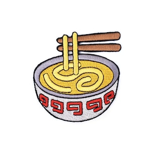 Puede incluir: Un tazón gris con ribetes rojos y amarillos lleno de fideos amarillos y palillos que sobresalen de la parte superior.