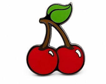 May include: A metal enamel pin shaped like two bright red cherries with brown stems and a single vibrant green leaf. The design features bold black outlines and white highlights on the rounded cherry fruits, creating a clean and graphic appearance.