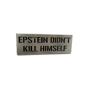 May include: A silver metal sign with the text "EPSTEIN DIDN'T KILL HIMSELF" in black lettering.