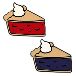 May include: Two enamel pins shaped like triangular slices of pie. One slice features a bright red filling, while the other has a dark blue filling. Both slices have a tan crust, a dollop of white whipped cream on top, and black outlines.