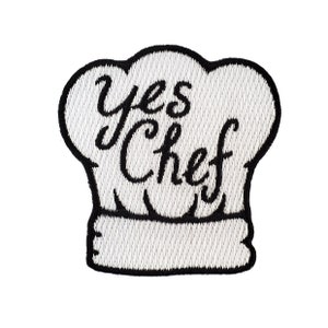 May include: White embroidered iron-on patch shaped like a chef's hat with the text "Yes Chef" in black.