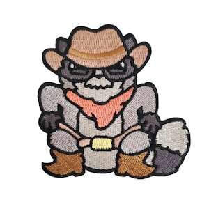 May include: Embroidered iron-on patch of a cartoon raccoon wearing a cowboy hat, bandana, and boots. The raccoon is sitting down with its arms crossed.