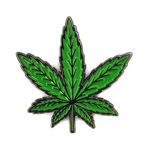 May include: A green marijuana leaf pin with a silver metal finish.