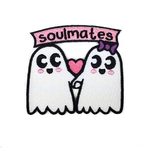 May include: Two white ghost figures with pink cheeks and black eyes holding hands with a pink heart between them. A pink banner above them reads "soulmates".