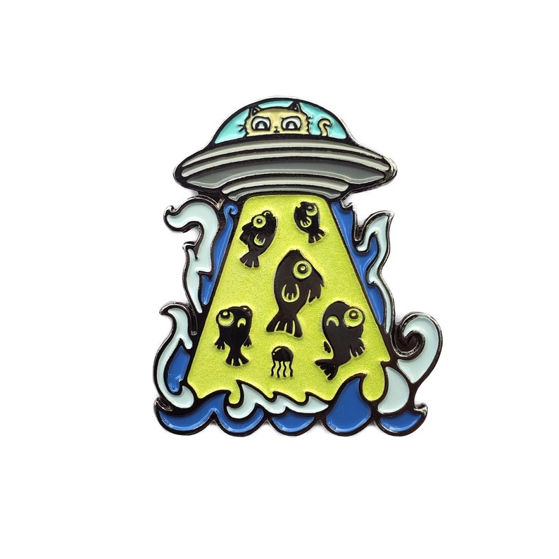 May include: A yellow and blue enamel pin featuring a cartoon cat in a flying saucer, abducting fish. The saucer is outlined in silver and the fish are black.