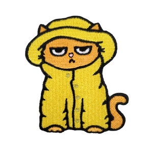 May include: An embroidered iron-on patch of a yellow cat wearing a yellow raincoat and hat. The cat has an orange face and a grumpy expression.