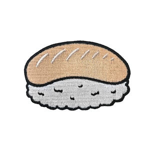 Puede incluir: Un parche bordado que representa un rollo de sushi. El sushi tiene forma de rectángulo con la parte superior e inferior redondeadas. La parte superior del sushi es marrón con líneas blancas, y la parte inferior es blanca con un diseño texturizado.