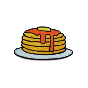May include: A stack of embroidered pancakes with orange syrup and a yellow pat of butter on a light blue plate.