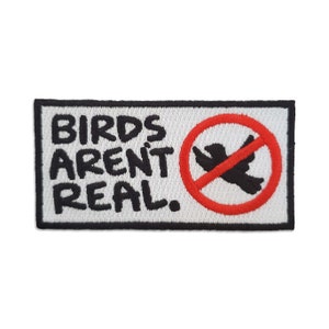 May include: White embroidered patch with black text that reads "Birds Aren't Real." A red circle with a diagonal red line through it contains a black silhouette of a bird.