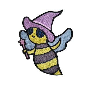 May include: An embroidered iron-on patch featuring a cartoon bee wearing a purple witch hat and holding a pink wand. The bee has yellow and black stripes and blue eyes. The bee has light blue wings.