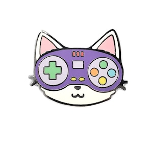 May include: Purple enamel pin of a cartoon cat wearing a purple video game controller with green, yellow, and blue buttons.