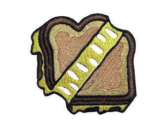 May include: A brown and yellow embroidered patch of a grilled cheese sandwich with a bite taken out of it.