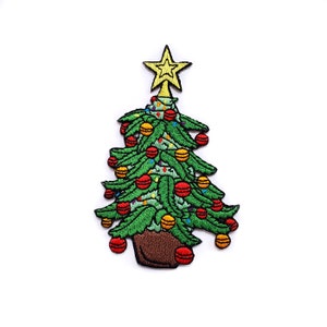 Puede incluir: Un parche bordado de un árbol de Navidad verde con una estrella amarilla en la parte superior y adornos rojos y amarillos. El árbol está en una maceta marrón.