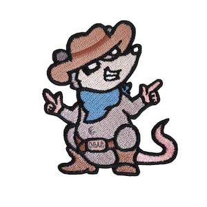 May include: A cartoon embroidered patch of a brown and gray mouse wearing a brown cowboy hat, a blue bandana, and brown boots. The mouse is holding a gun in its right hand and has a peace sign with its left hand. The mouse has a pink tail.