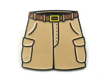 Può includere: Uno spillo in smalto marrone a forma di pantaloncini cargo color kaki con cintura marrone e cuciture nere.