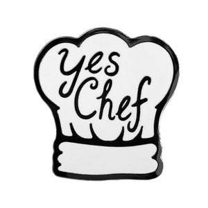 May include: White enamel pin shaped like a chef's hat with black outline and the text "Yes Chef" in black.