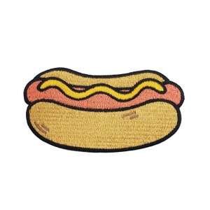 May include: A cartoon-style embroidered patch of a hot dog with yellow mustard on a bun.