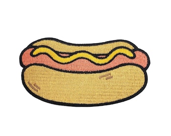 May include: An embroidered patch shaped like a hot dog. The design features a tan bun, a pinkish-red sausage, and a wavy line of bright yellow mustard across the top. The entire graphic is outlined in a thick, bold black thread border.