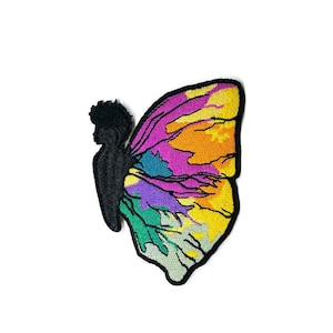 May include: A colorful embroidered patch featuring a butterfly with a silhouette of a person in the center. The butterfly's wings are a mix of yellow, orange, pink, purple, green, and blue.