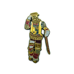 May include: A gold-colored enamel pin depicting a whimsical figure wearing a hat and holding a stick. The figure is dressed in a colorful outfit with intricate details. The pin is a fun and quirky accessory.