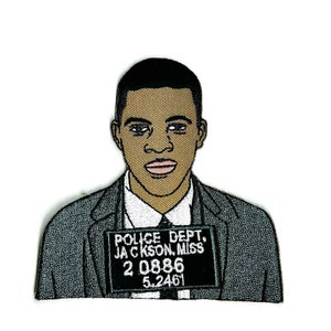 May include: Embroidered patch of a man in a suit with a police mugshot. The mugshot reads "Police Dept. Jackson, Miss. 20886 5.2461".